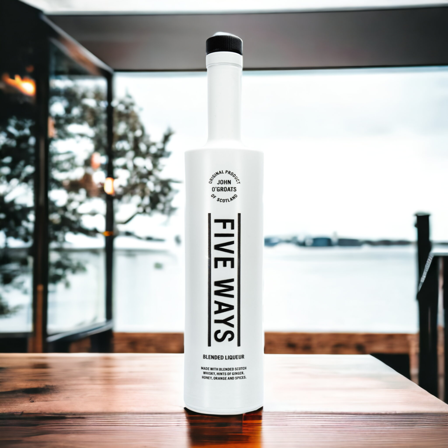 Tall slim white bottle with black writing on wooden plinth with outdoor scene in background. Whisky liqueur.